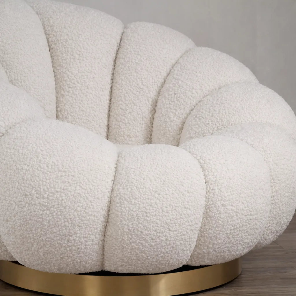 Poltrona Elodia in tessuto bouclé color panna con seduta avvolgente e base circolare in metallo color oro